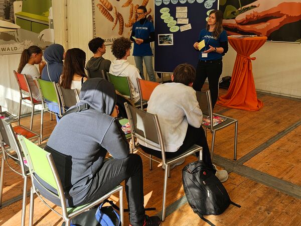 Dr. Susanne Weiß-Wittstadt und Yasmin Leibenath vor Schüler:innen im EMPOWER-Zelt auf dem Mainzer Wissenschaftsmarkt