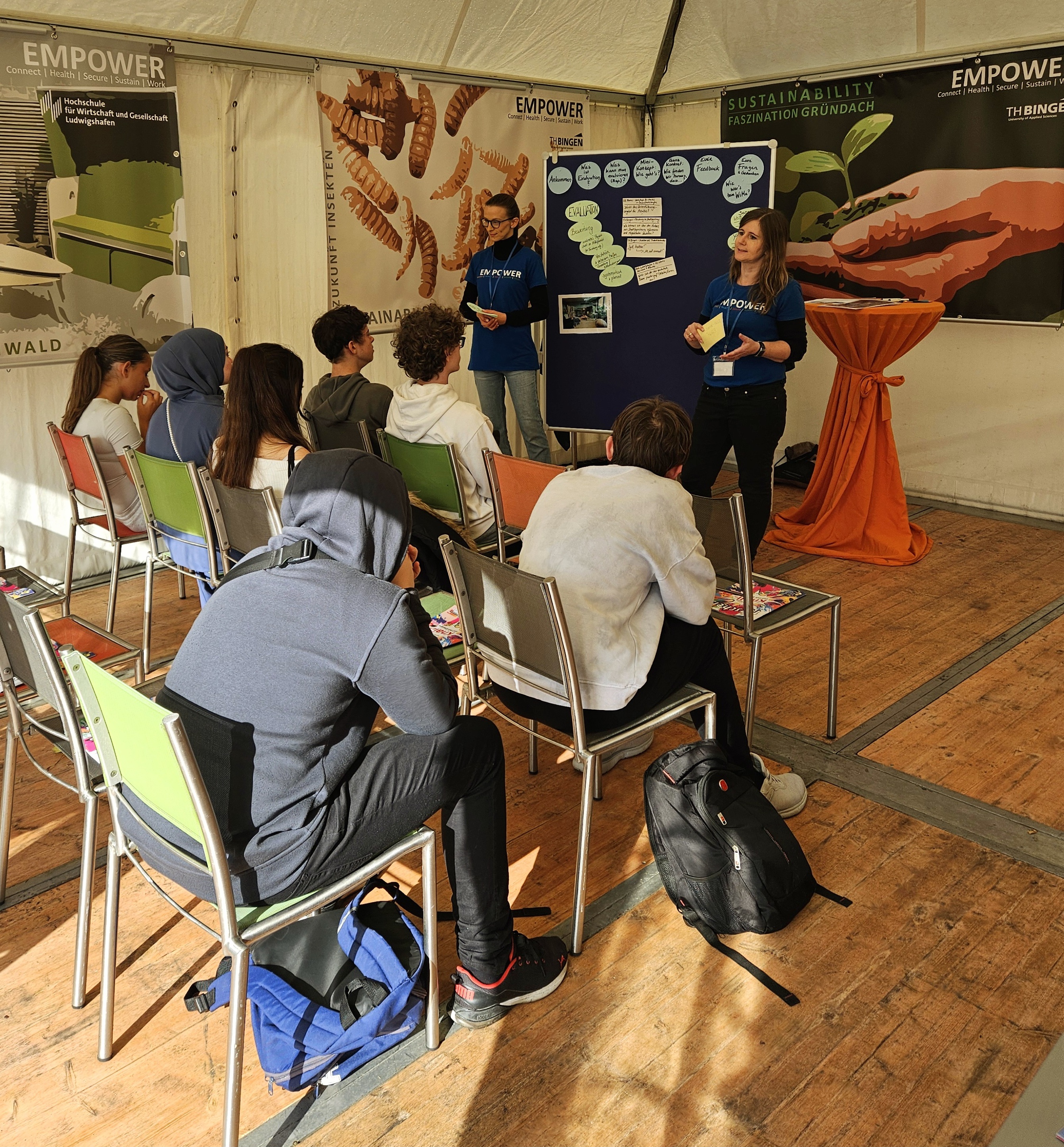 Dr. Susanne Weiß-Wittstadt und Yasmin Leibenath im EMPOWER-Zelt auf dem WIMA vor Schüler:innen der 9. und 10. Klasse, die sie in das umfangreiche Thema „Evaluation“ einführen.